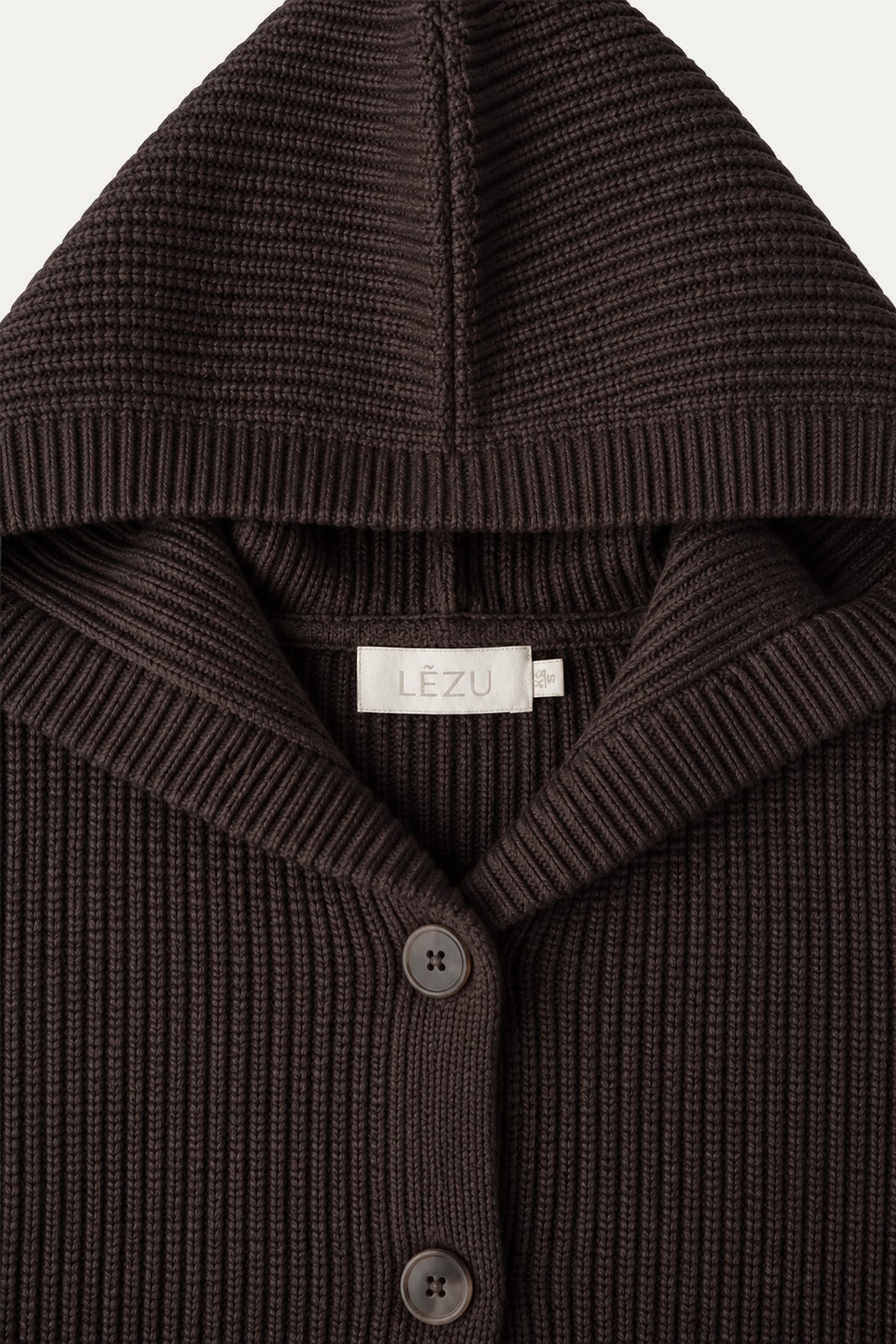 Detailaufnahme einer dunkelbraunen Strickjacke mit Kapuze, geripptem Kragen, braunen Knöpfen und hellem LEZU-Label.