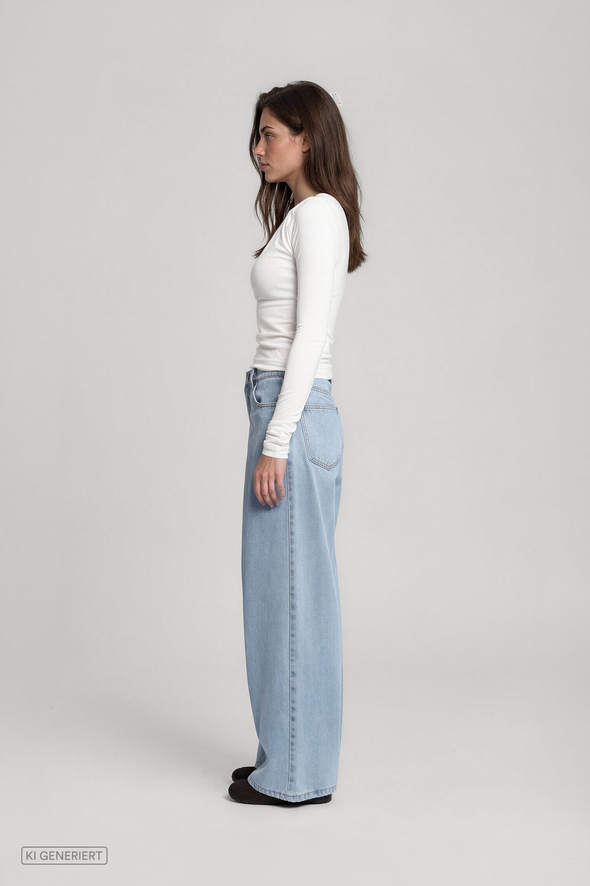 Seitenansicht eines Models in einem weißen, langärmeligen Oberteil und einer hellblauen, weit geschnittenen Jeans.