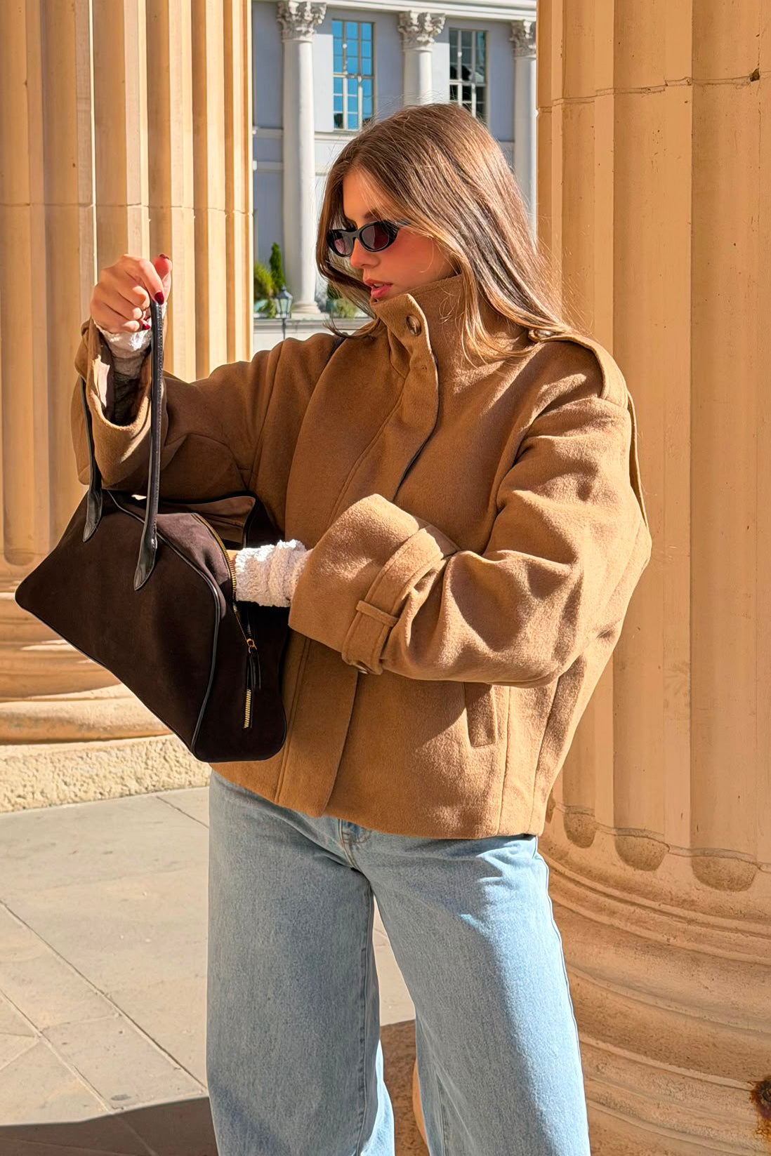 Model trägt die NALU Jacke in Beige von LEZU – weite Hemdjacke aus Wollmix mit Stehkragen und Ärmelriegeln, kombiniert mit heller Jeans und brauner Tasche