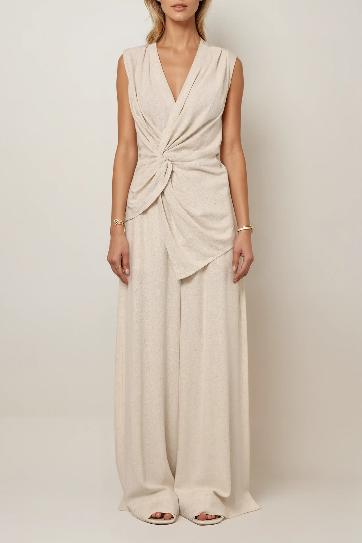 Model trägt ein ärmelloses, drapiertes Top mit Knotendetail und V-Ausschnitt, kombiniert mit einer weit geschnittenen Hose in passender Farbe.