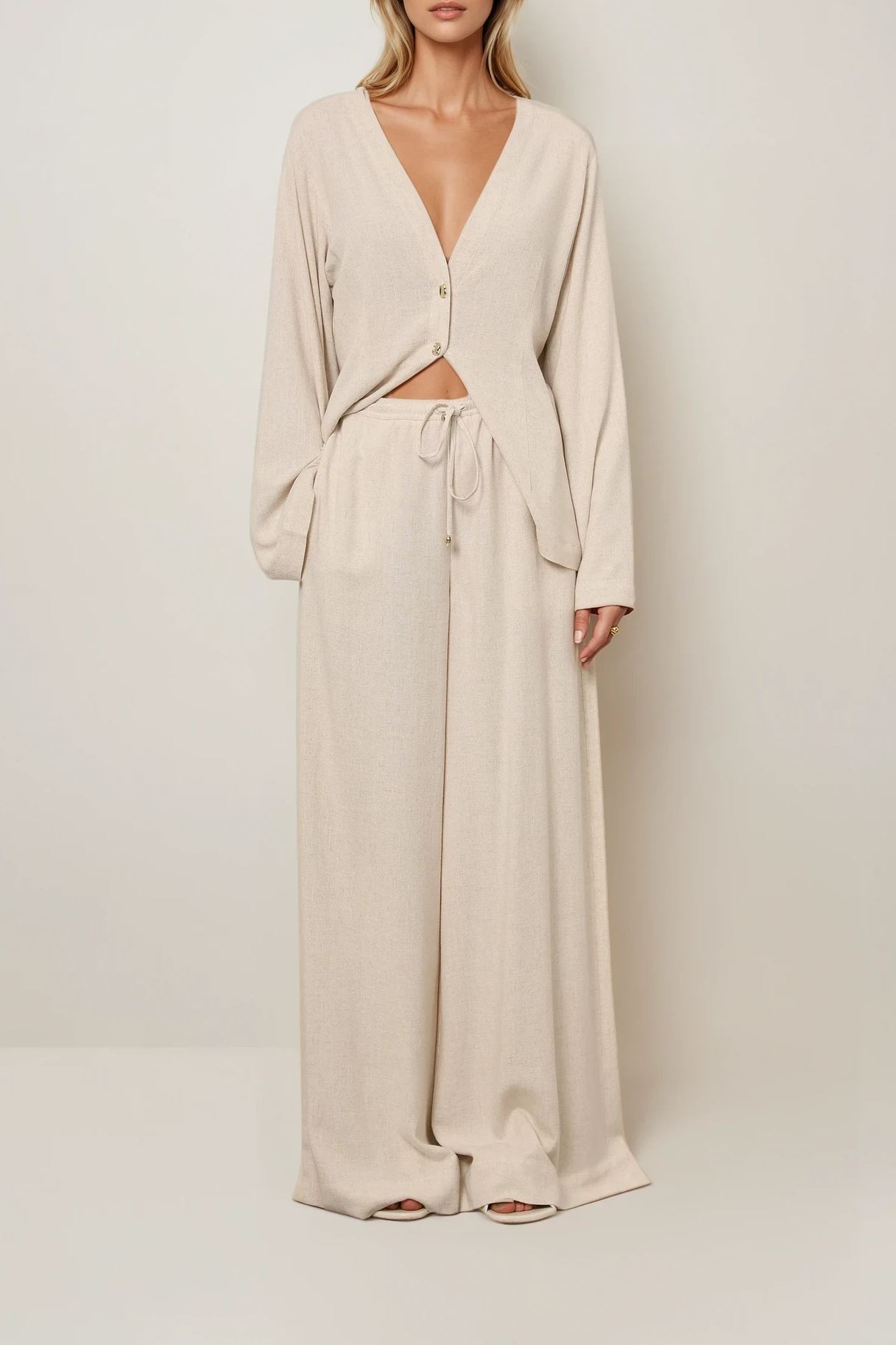 Model trägt eine weit geschnittene Hose in Beige Melange mit Tunnelzug, kombiniert mit einer locker fallenden Strickjacke.